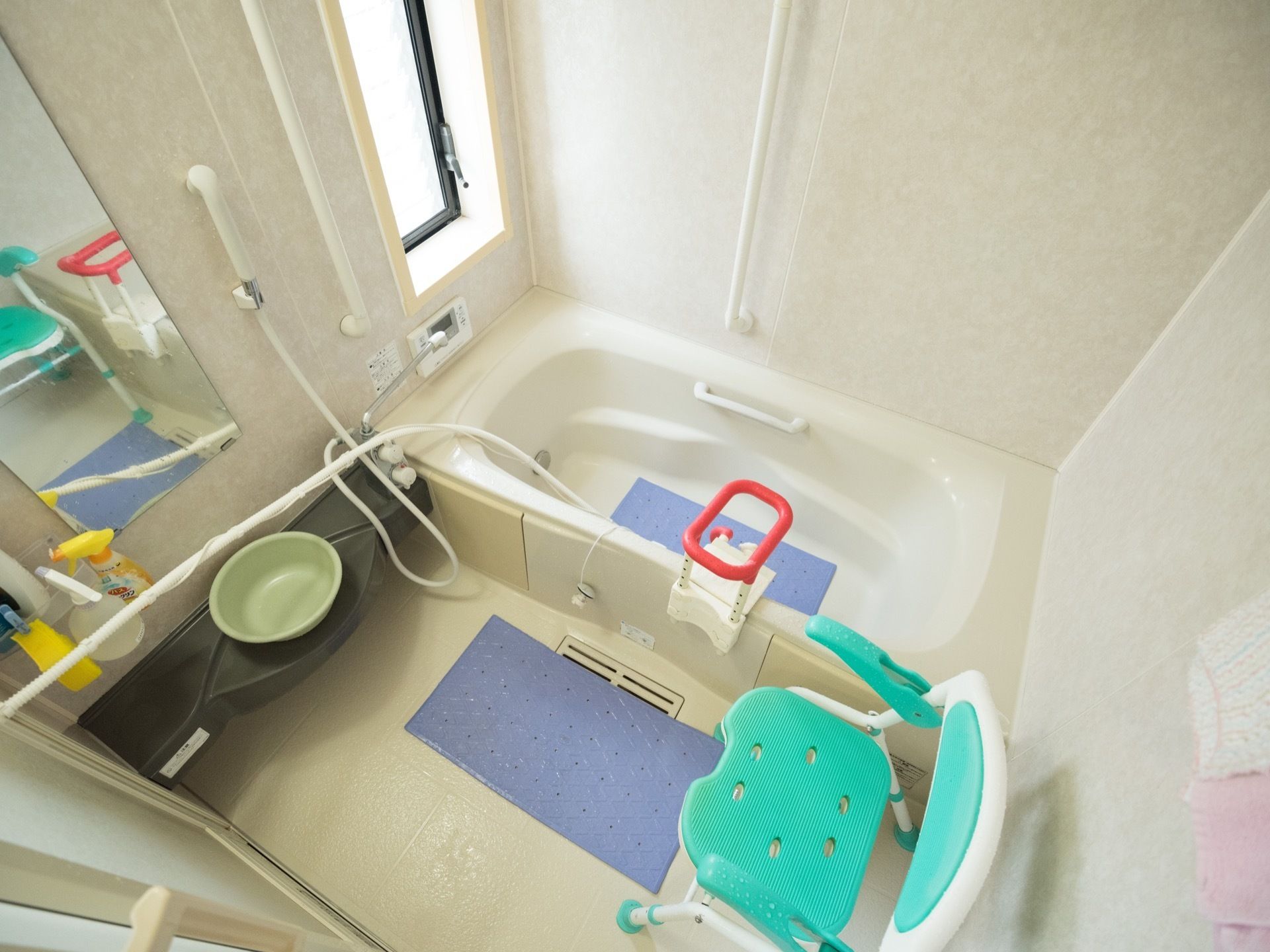 白を基調とした、シンプルな浴室である。滑り止めマットが敷かれているほか、シャワーチェアや手すりも設置されている。