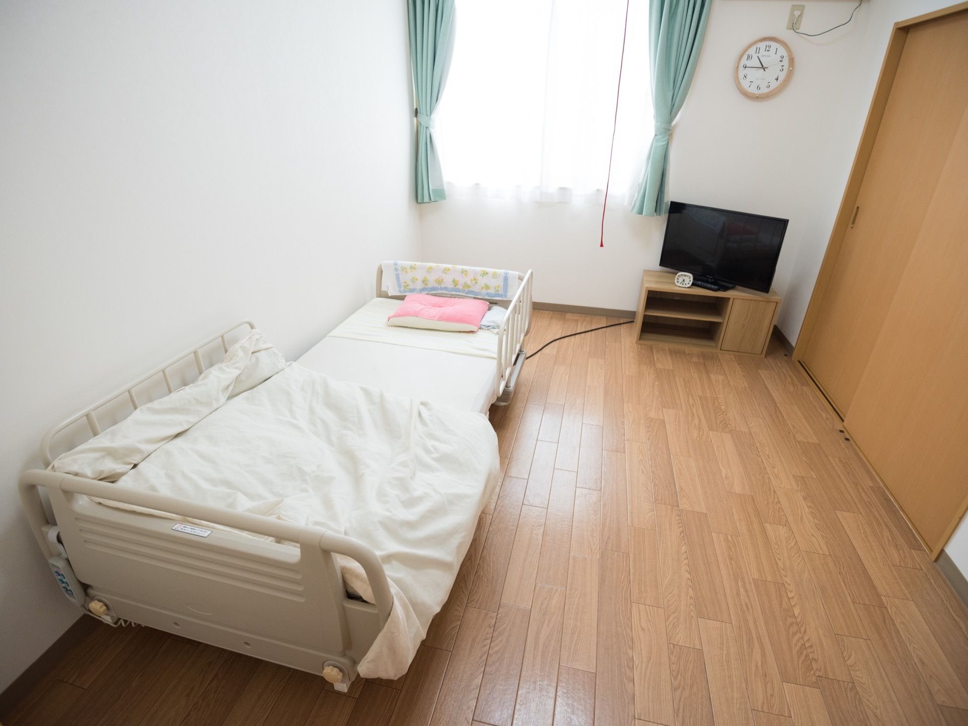 木のぬくもりただよう、シンプルな居室である。白色の介護専用ベッドが置かれている。窓側にはテレビがある。