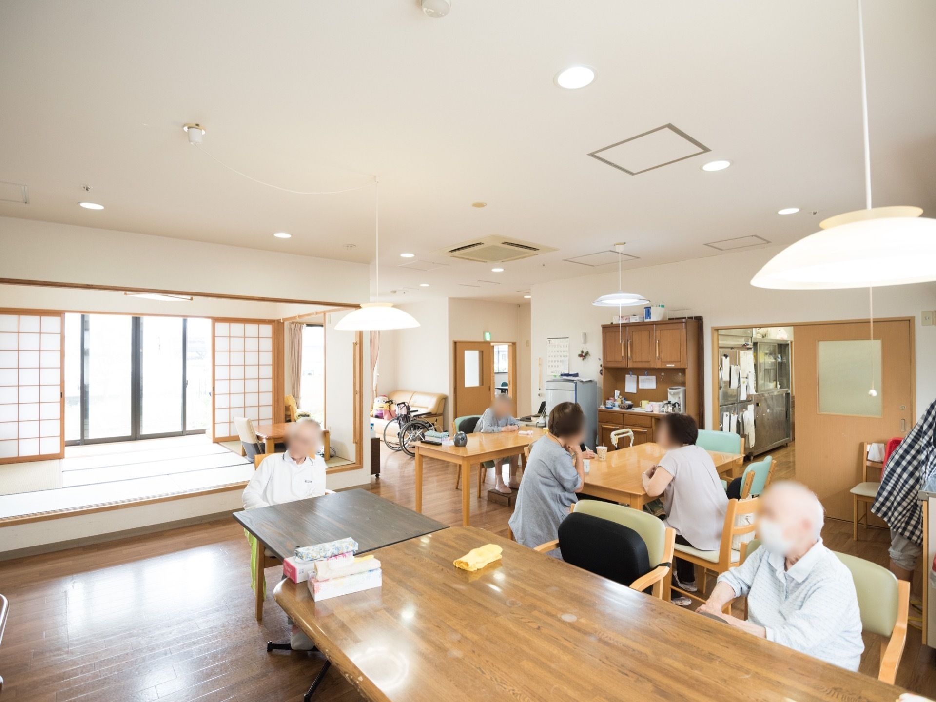 和室と洋室が混在する、広々とした共有スペースである。つり下げタイプの照明が、複数設置されている。テーブルもある。