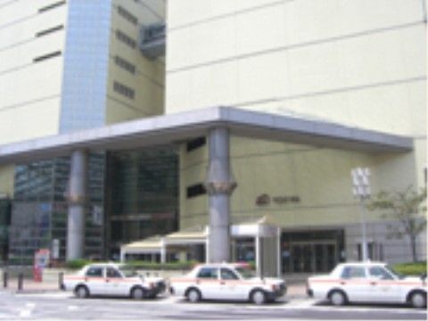 近隣の百貨店の外観である。入り口には大きな円柱形の柱に支えられた張り出した屋根がある。その前にはタクシーが並んでいる。
