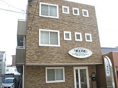 ブラウン系の3階建ての建物。玄関部分には屋根が付いていて、建物外壁にホーム名がある。