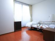 部屋の奥には、カーテンつきの窓がある。ベッドが置かれており、その脇には棚がある。ランプも設置されている。