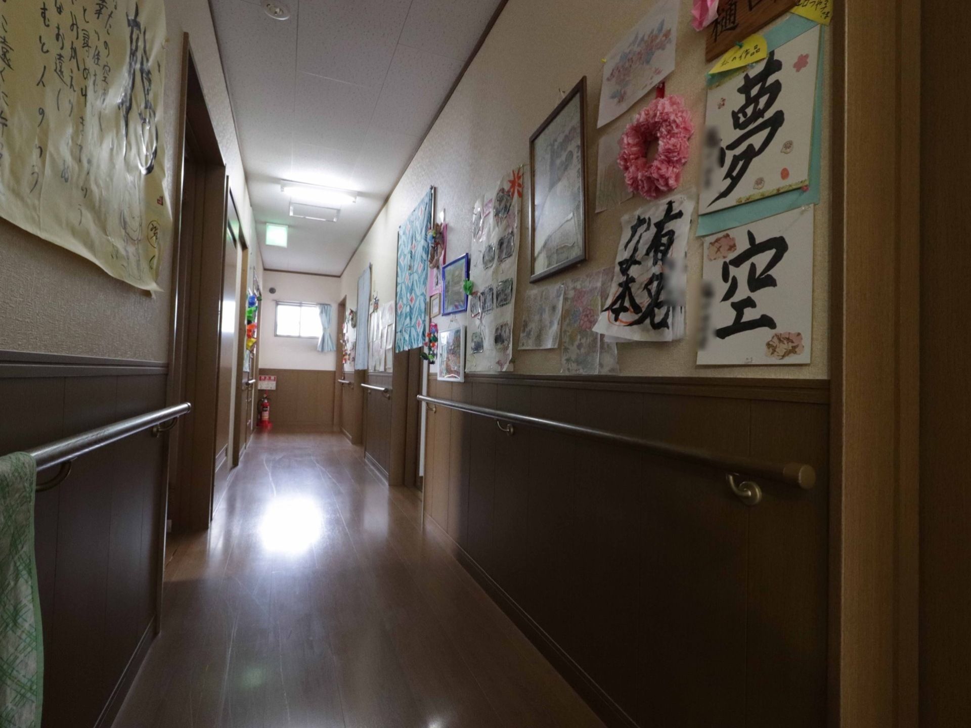 施設の廊下。壁に掲示物が数多く飾られており、安全のための手すりが付いている。床もバリアフリーで清潔に保たれている。