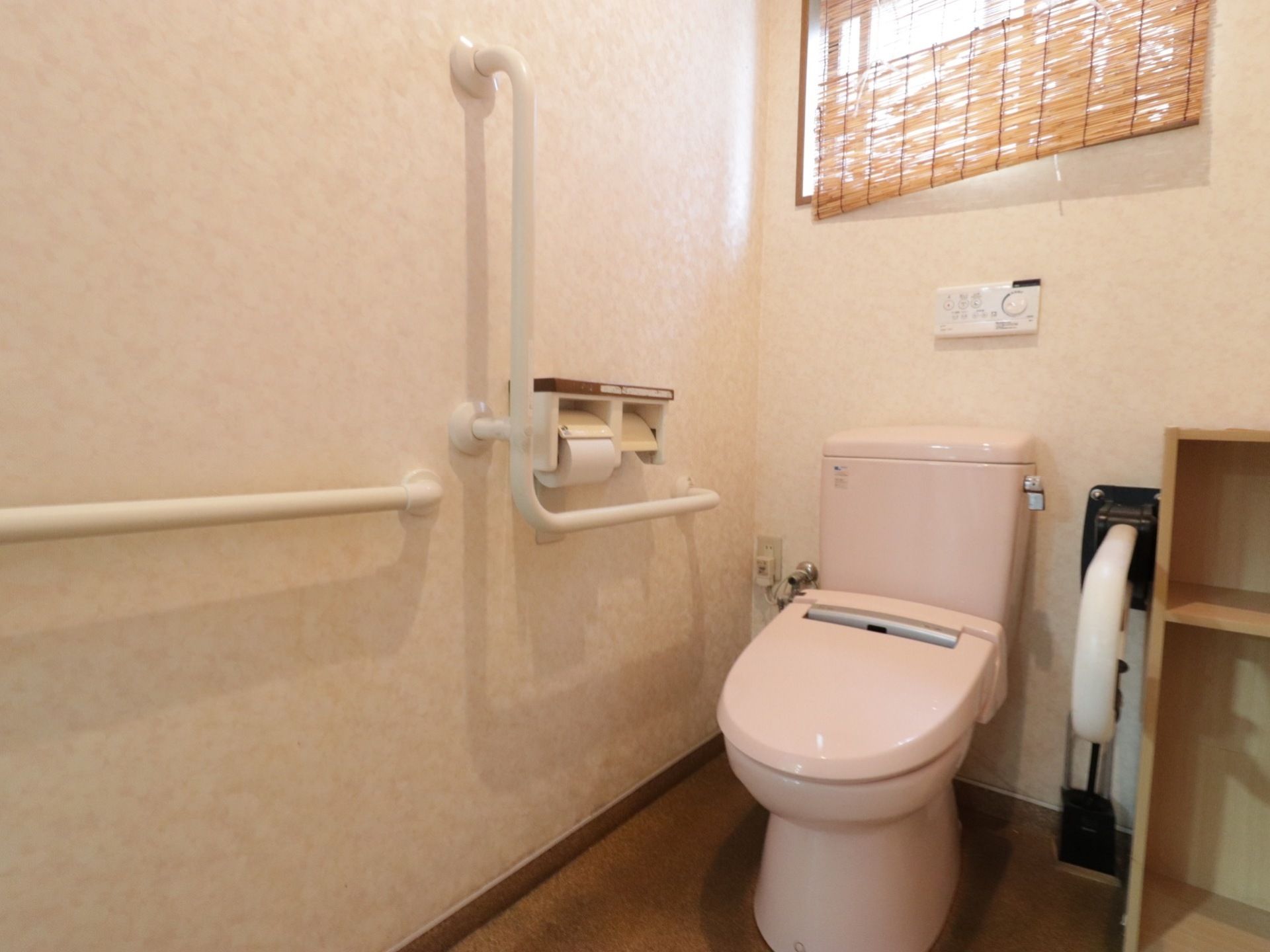 洋式トイレでⅬ字型とI型の手すりが壁に取り付けてある。窓があり明るい。雑貨を置くことのできる棚も備えている。