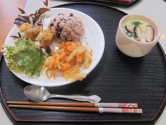 かき揚げやしその天ぷら、赤飯、そして茶碗蒸しが並んだ半月型の黒いトレーにはスプーンと箸も添えられている。