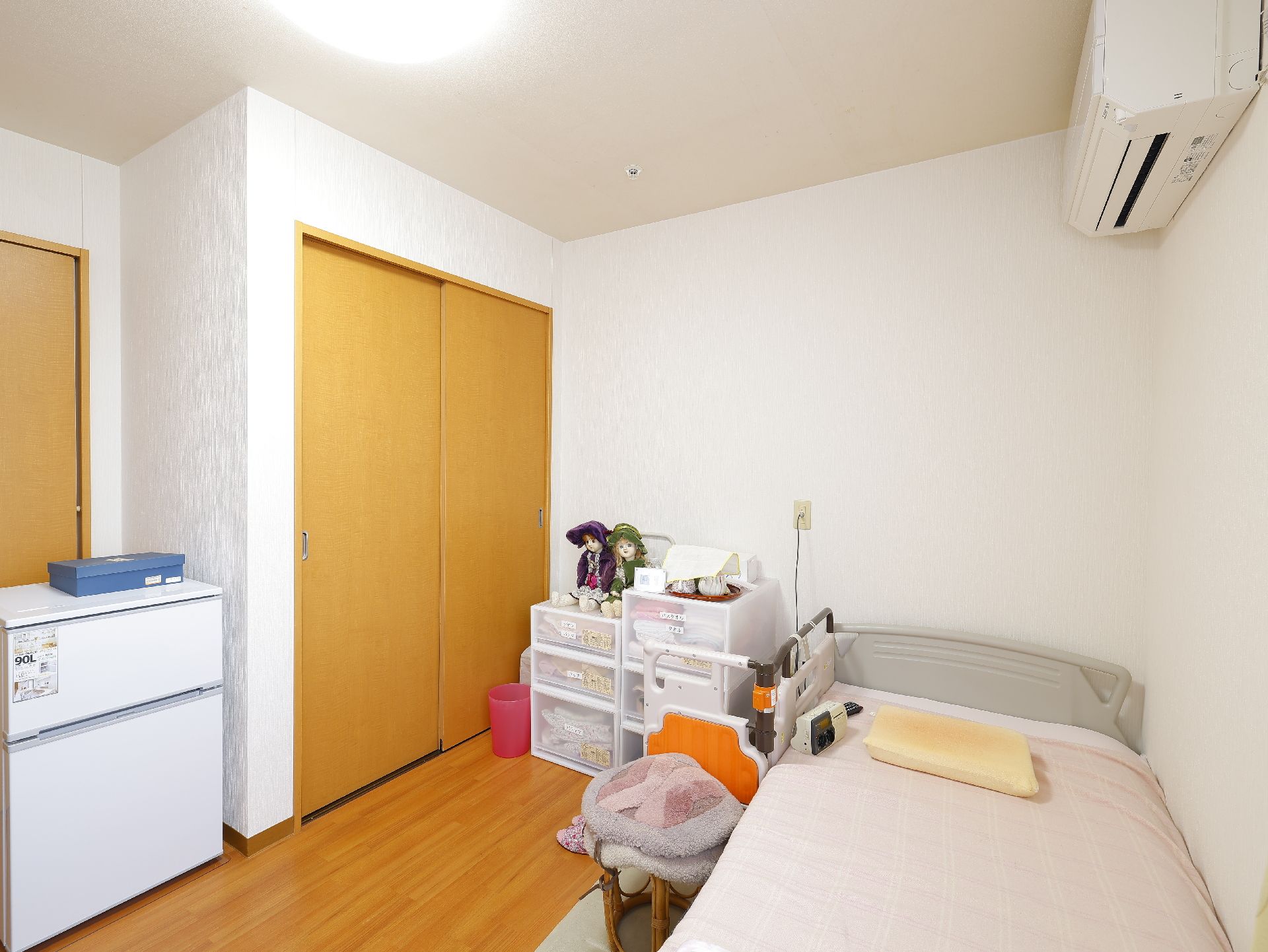 介護ベッド、秋桜、小型の冷蔵庫などが置かれている居室