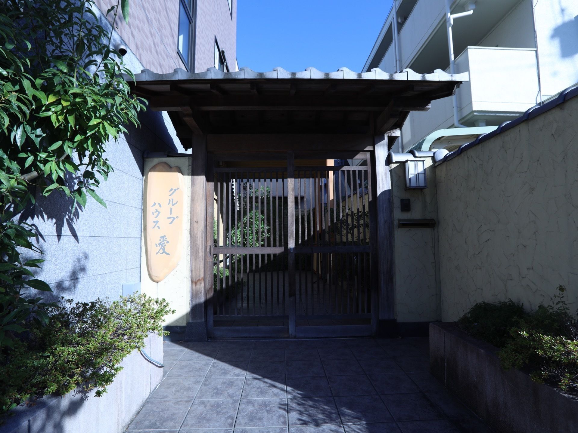 施設の玄関前には、瓦と木で作られた門が設置されている。左側には、大きな一枚板に施設名の書かれた表札が掛けられている。