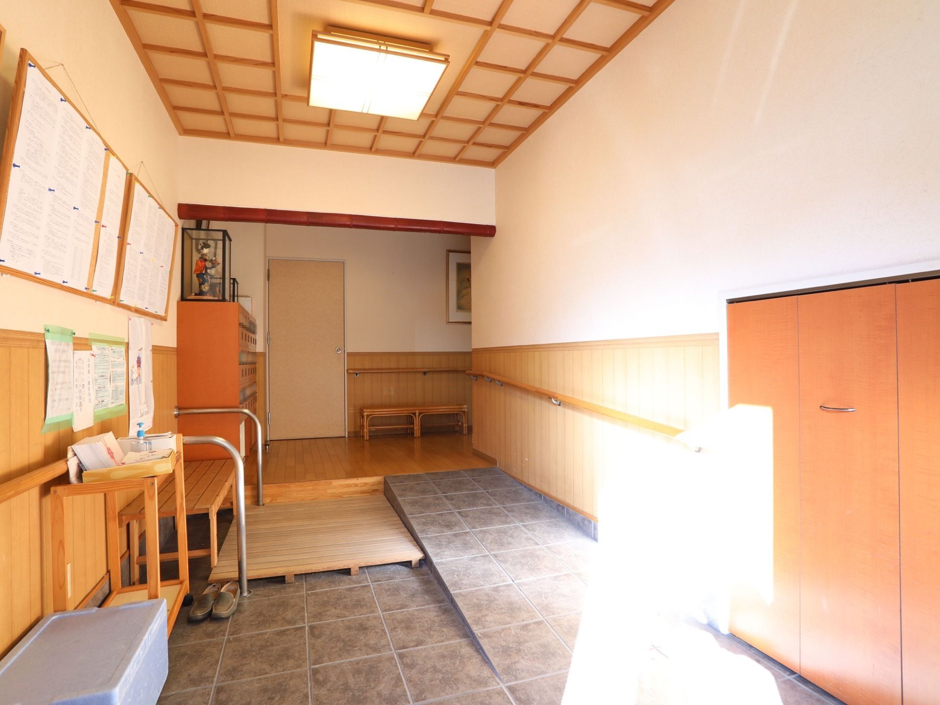 玄関には、木造のベンチとすのこが置かれている。廊下に繋がる壁には、茶色い手すりが取りつけられている。