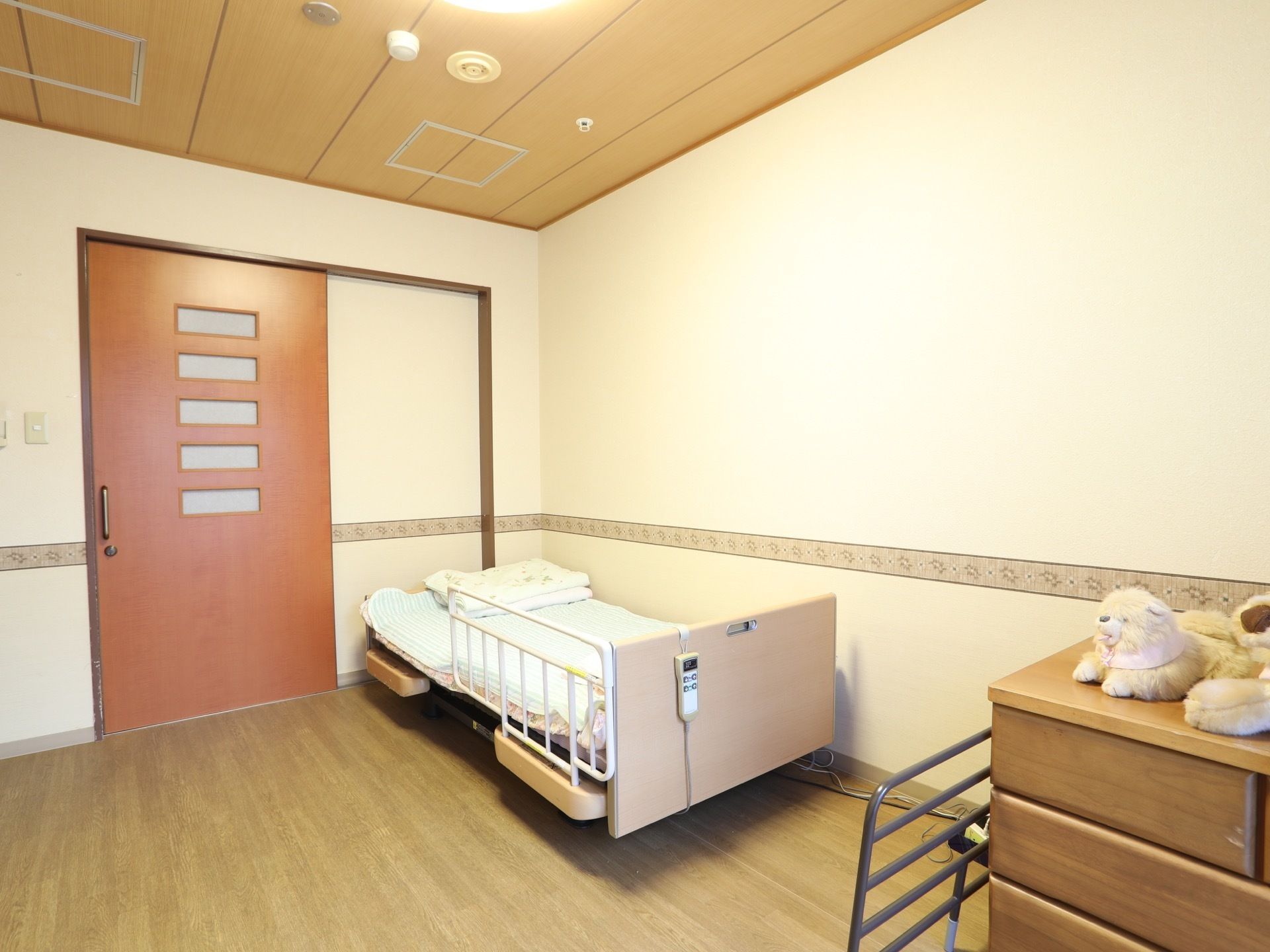 居室はゆったりとした広さがあり、入口には引戸が取りつけられている。右側にはベッドが置かれていて、タンスもある。