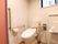 室内には、タンク付きのトイレが設置されている。壁には茶色い手すりがあり、ピンク色の扉が取りつけられている。