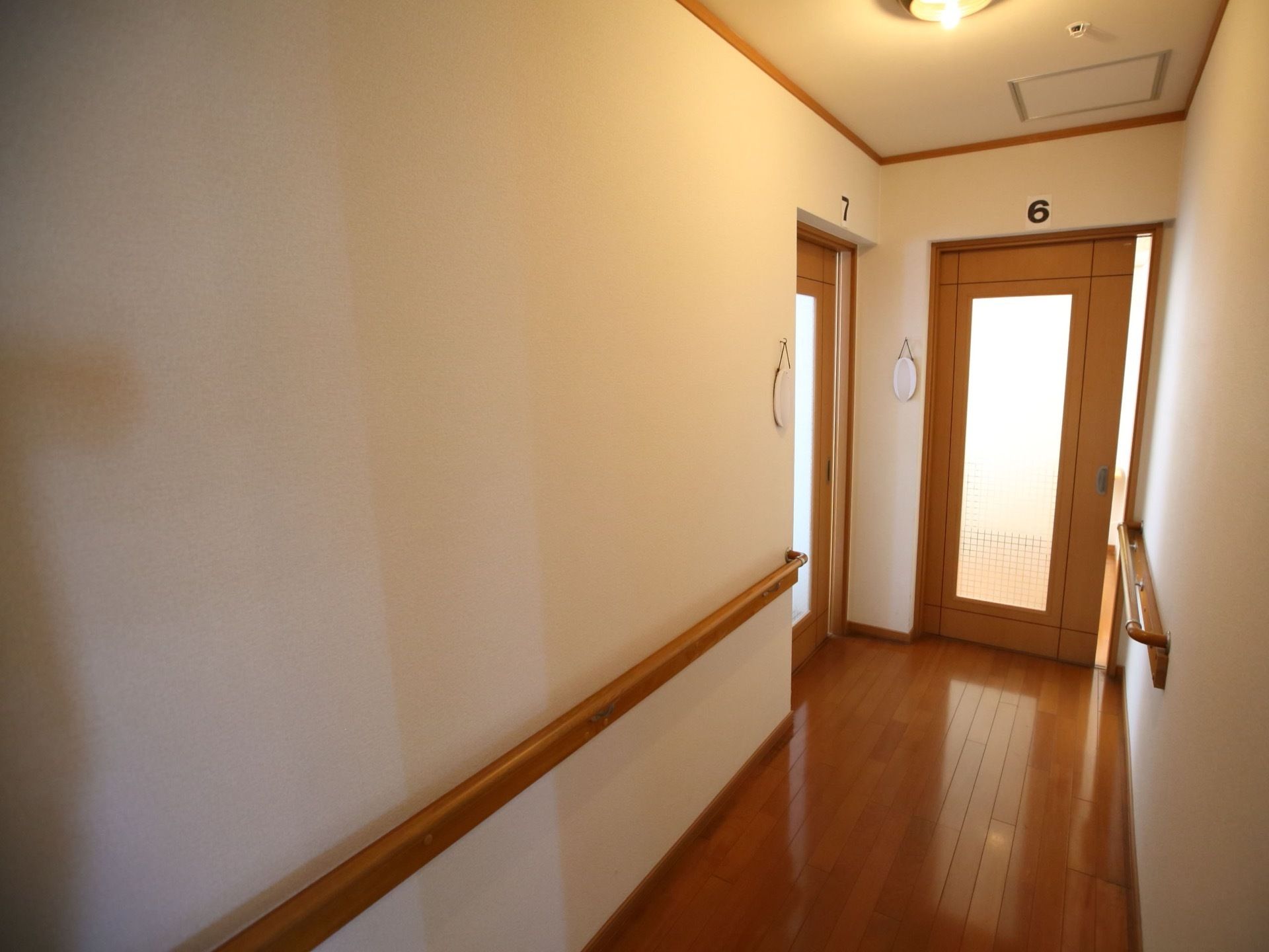 フローリングの床の通路があり、通路の行き止まりと左の壁に１つずつ引き戸の扉がある。通路の壁には手すりが備えられている。