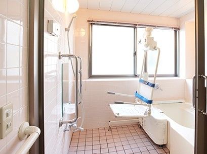 リフト浴が設置された浴室。白い浴槽が右手、手すり付きのシャワーが左手にある。