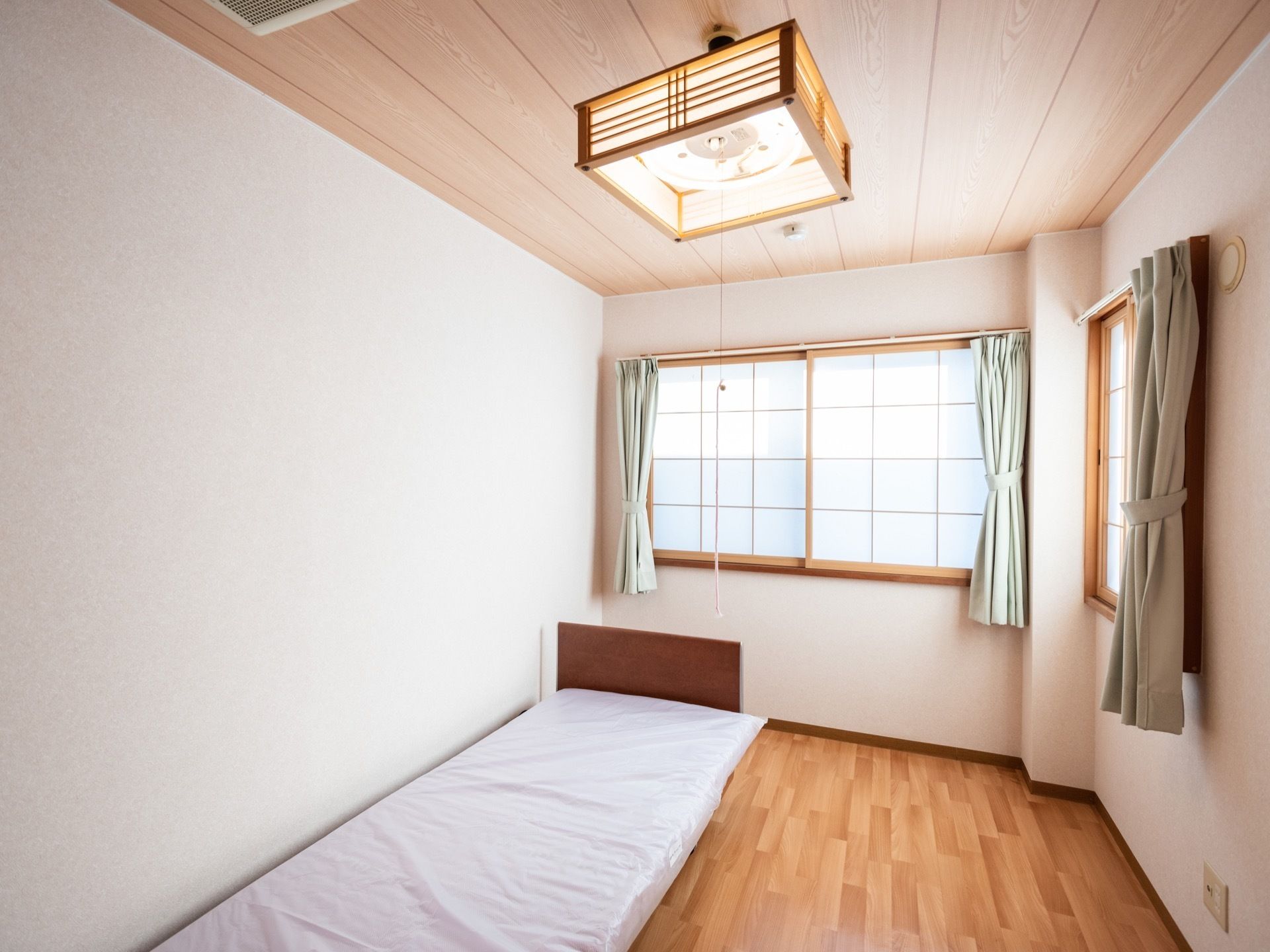 廊下側から居室内を見た画像である。奥と右側に障子が嵌められた窓が２か所にある。天井には照明が下がっている。