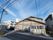 三角屋根の２階建ての施設が中央に建っている。施設の前は歩道になっており、街路樹や街頭がある。左手に駐車場がある。