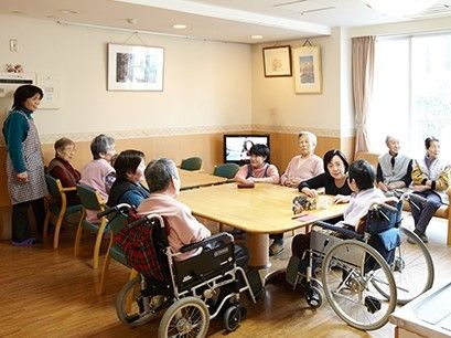 木製のダイニングテーブルを囲んでスタッフと入居者が穏やかに過ごしている様子。