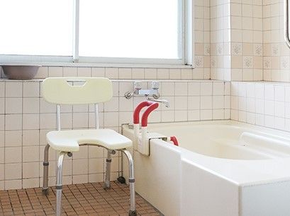 一般の家庭と同じようなサイズの浴槽が置かれた白い浴室にはシャワーチェアと手すりも設置されている。