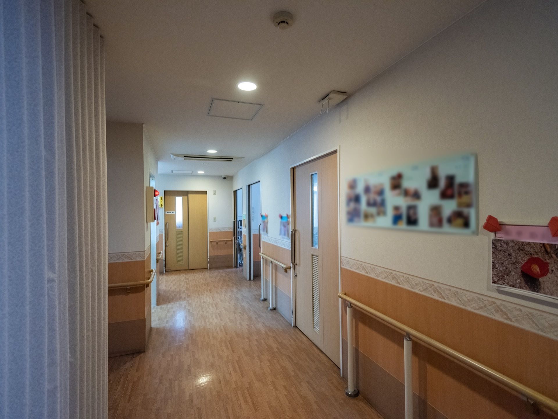 フローリングの床の通路には手すりがある。入居者様の作品や、行事での写真を展示している。火災報知器を設置し、災害時に備えている。