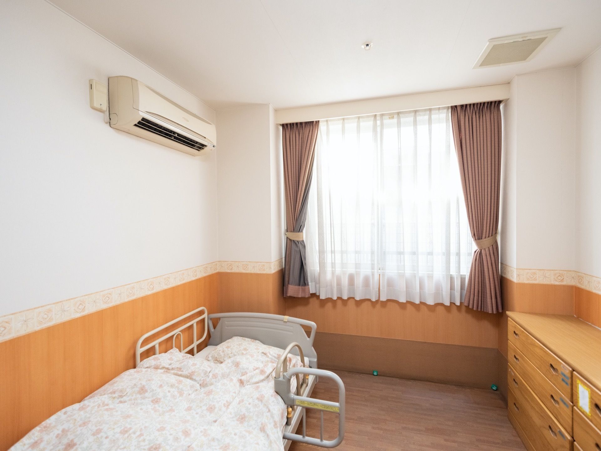 居室には大きな腰高窓があり、部屋の雰囲気に合うカーテンを備えている。ベッドには柵を設置し、ベッドへの移動など安全にできるように配慮している。
