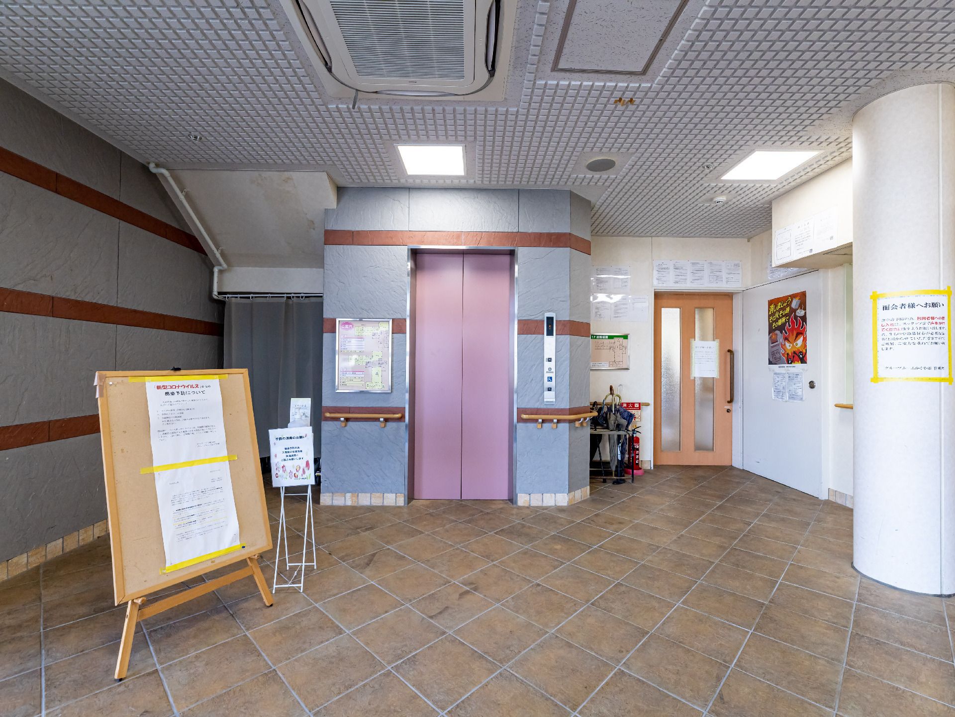 緑の多い屋外で笑顔で散歩をしている車いすの高齢女性と付き添いのエプロンを付けた女性スタッフ。