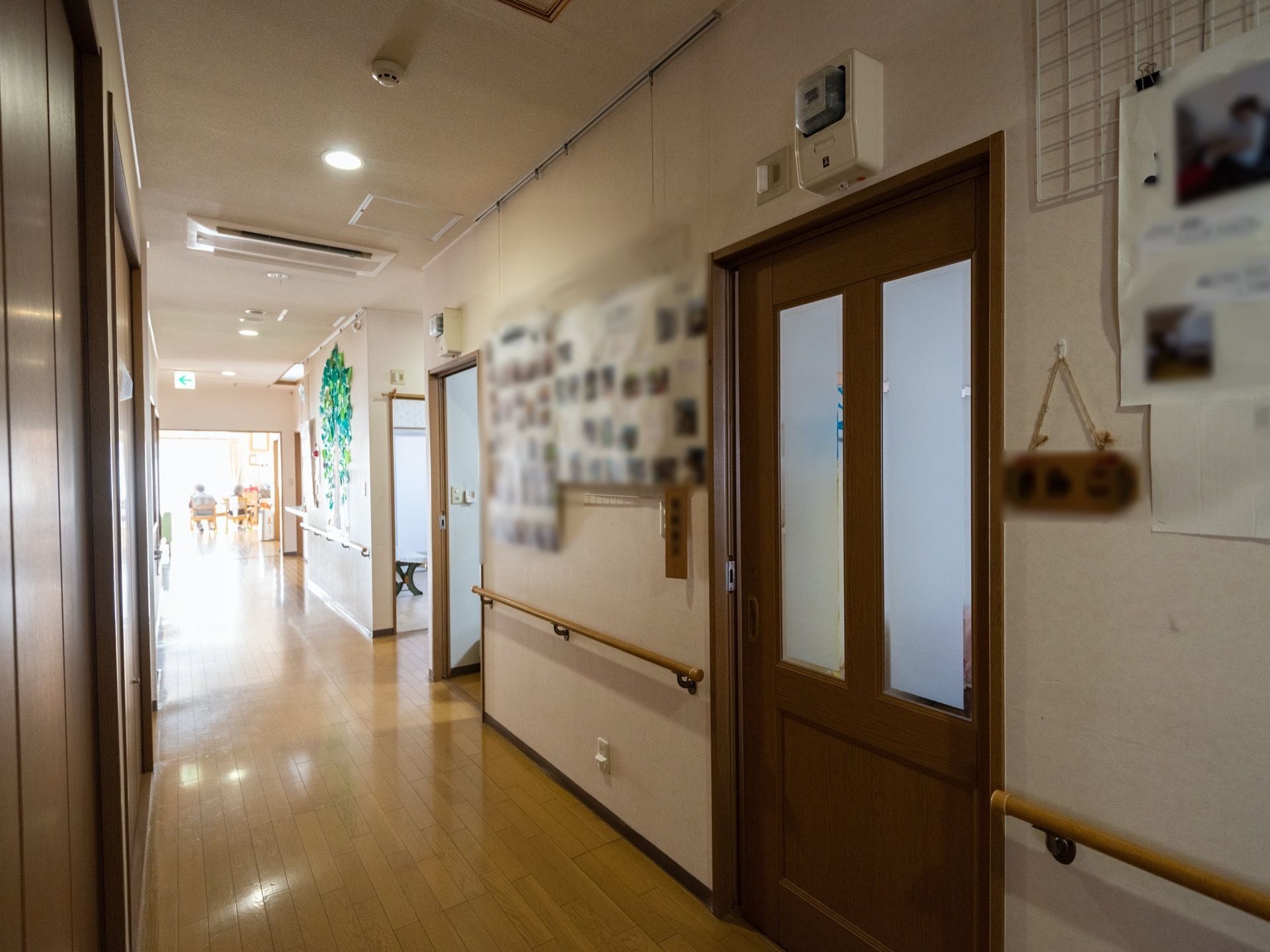 ビルトインのエアコンが完備された居室前の廊下である。手すりが設置された白い壁には、記念写真や飾り付けがされている。