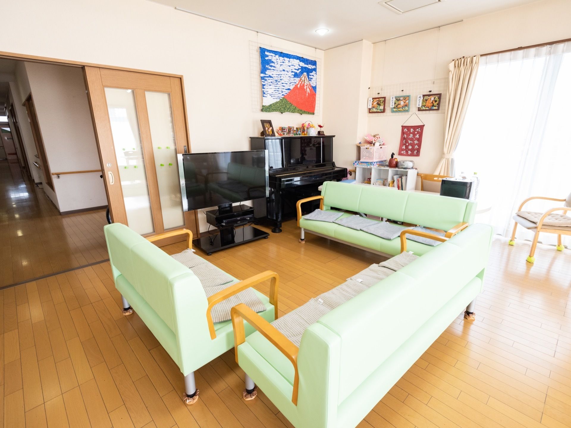 リビングではテレビやピアノが設置されている。白い壁には日本一高い山のタペストリーが上部に掛けられている。