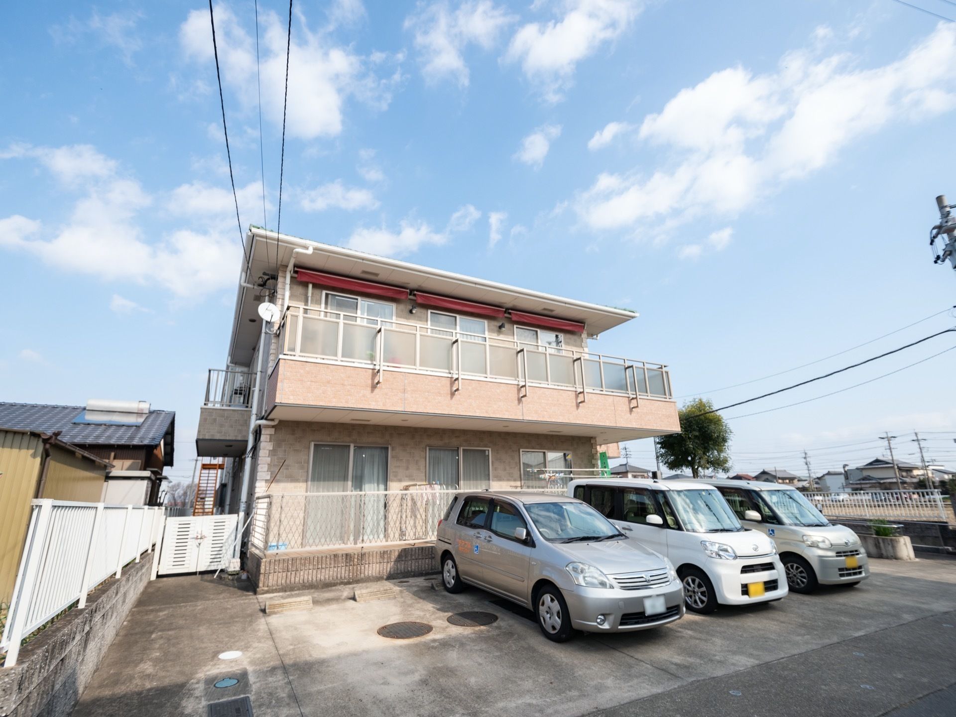 ベランダが完備された2階建ての施設である。所有している駐車場スペースには、3台の乗用車が停車している。