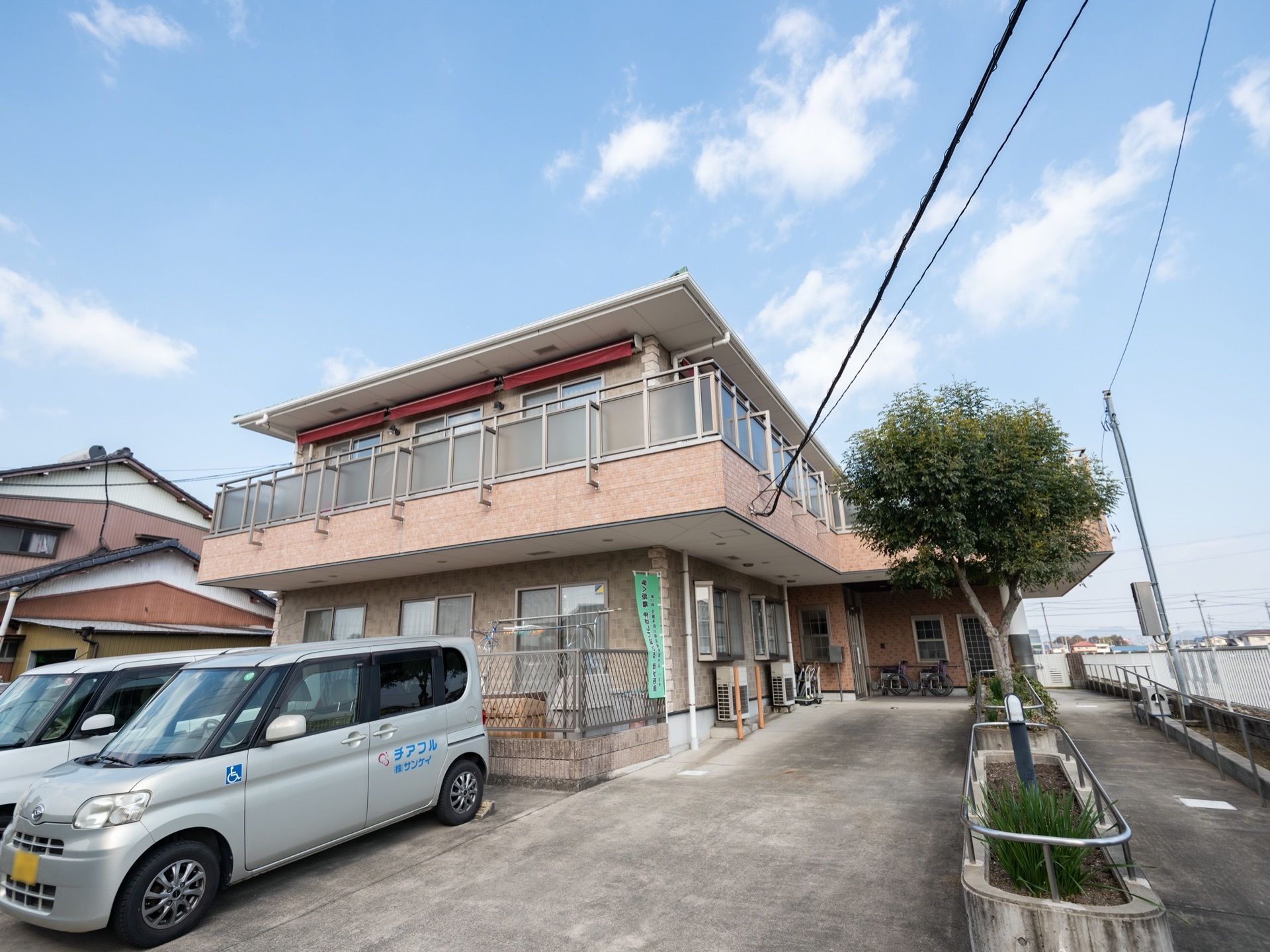ベランダと駐車場スペースを完備した、2階建て施設の外観である。緩やかな勾配が施設入口へと続いている。