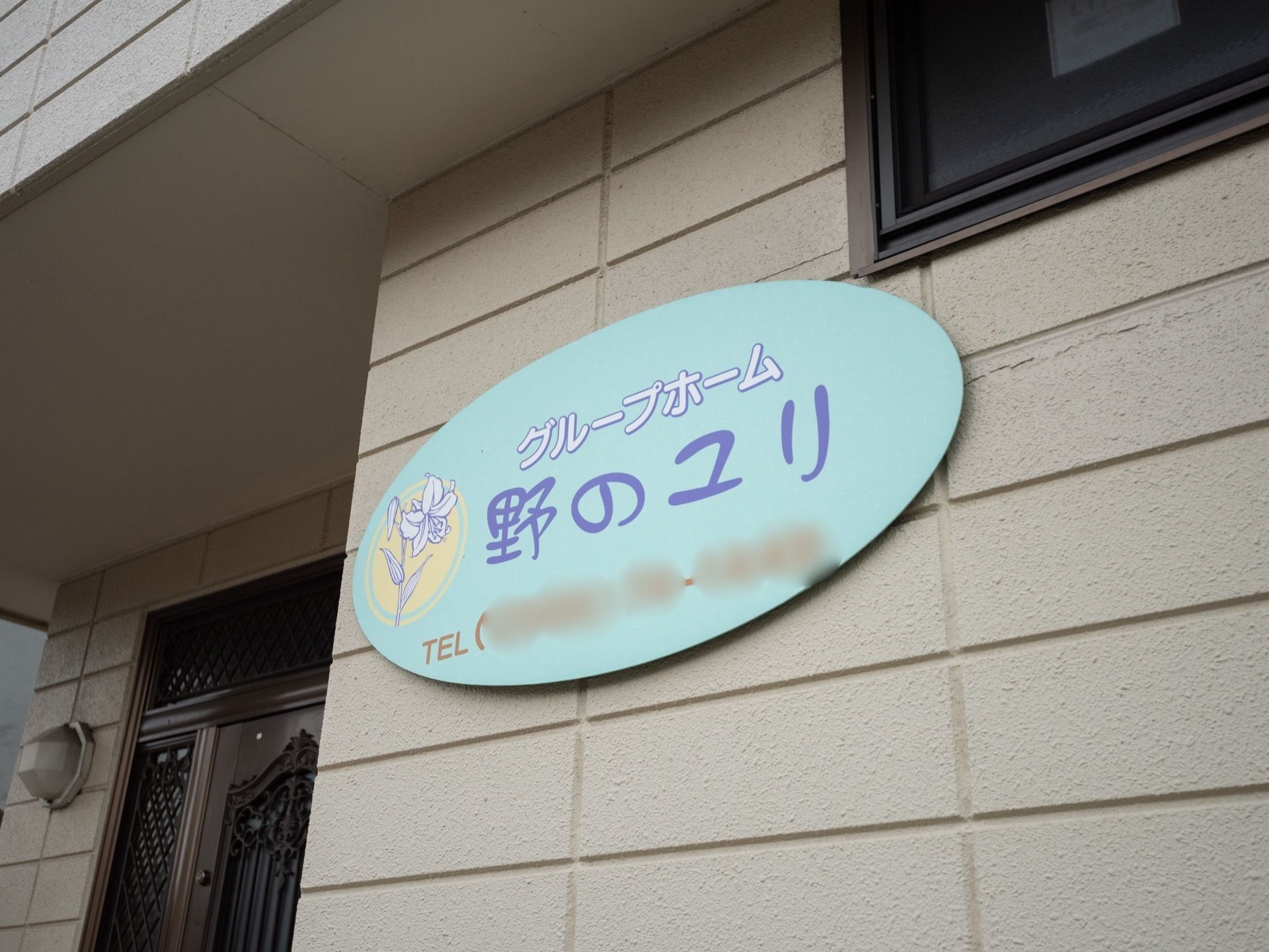 玄関の横に飾られている施設名が書かれた看板である。全体が水色になっていて、名前にちなんだユリの花の絵も白色で描かれてある。