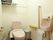 小花模様の壁紙が使われたトイレである。ピンクの便器があり、壁には手すりがある。個室内に手洗い場が備わっている。