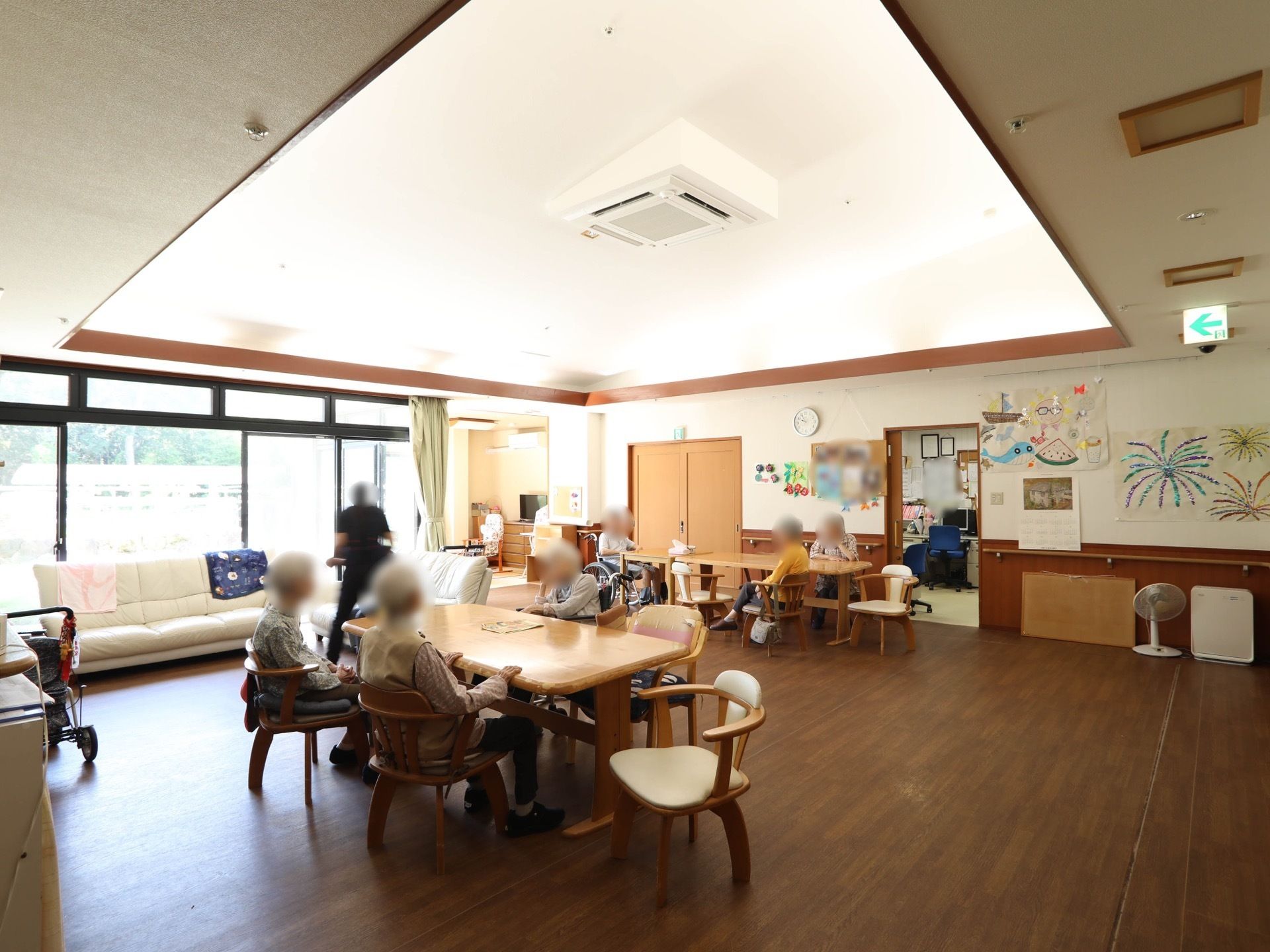 天井には間接照明が施された、リビングテーブルやソファーが置かれた共有スペース。入居者様が思い思いの場所でくつろいでいる。