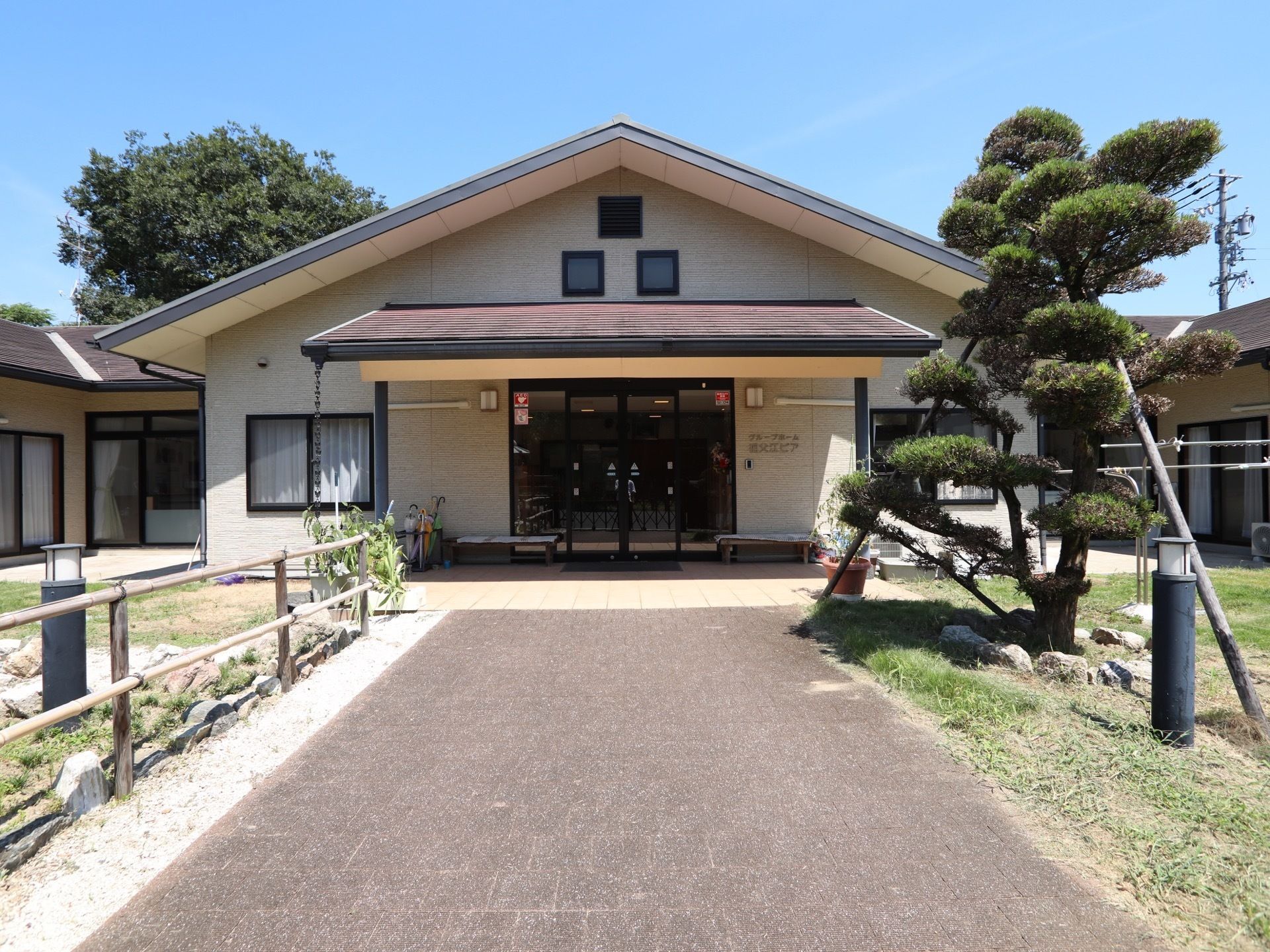 大きなひさしがある玄関である。ひさしの下にはベンチや傘立てがある。駐車場からの道は石畳のようになっている。