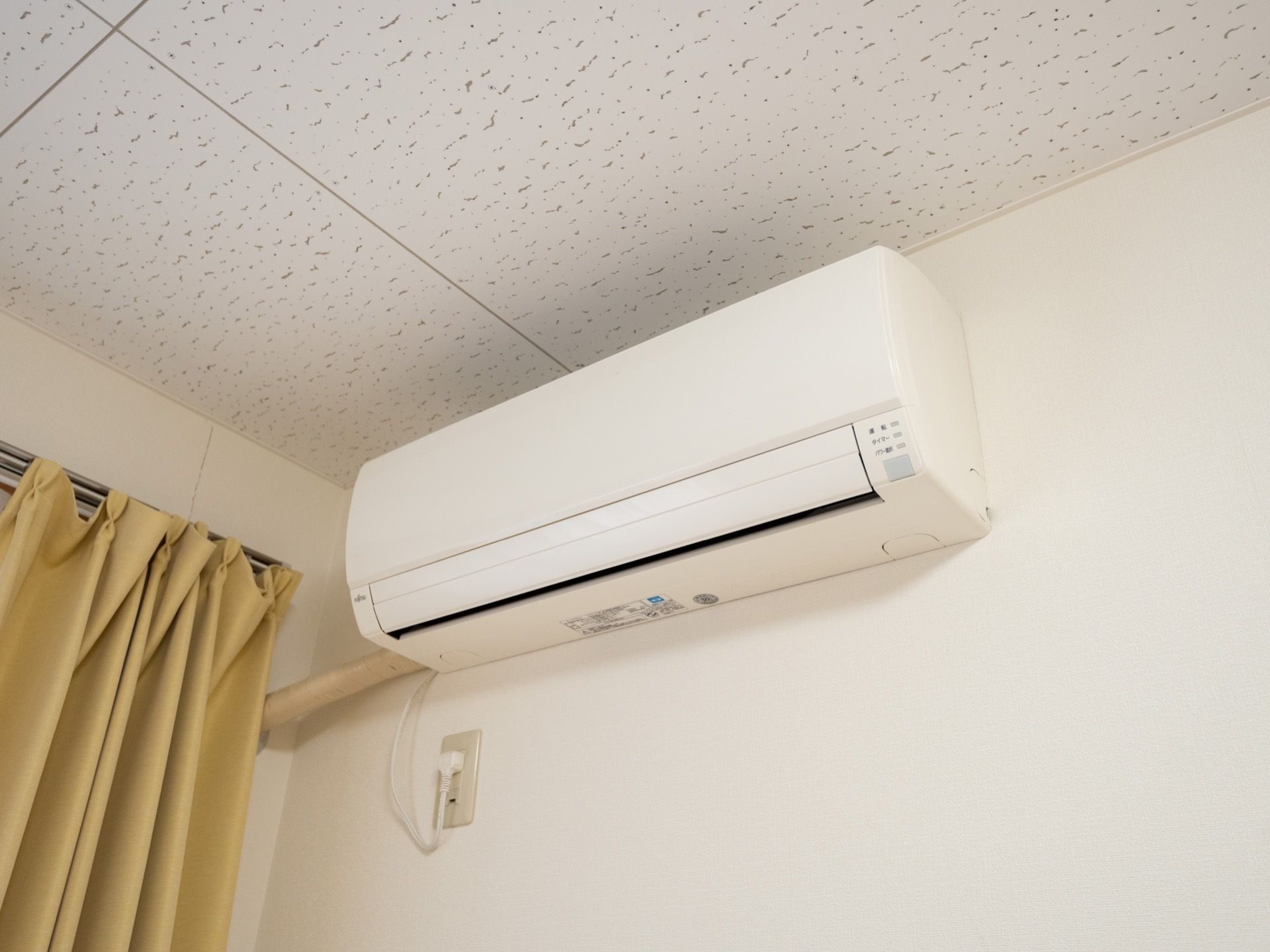 居室の高い位置に家庭用エアコンが設置されている。白色の外装は壁紙にマッチしている。専用のコンセントに接続されている。