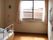 レースカーテンとカーテンが付いた窓があるフローリングの部屋には寝具付きのベッドが置かれている。