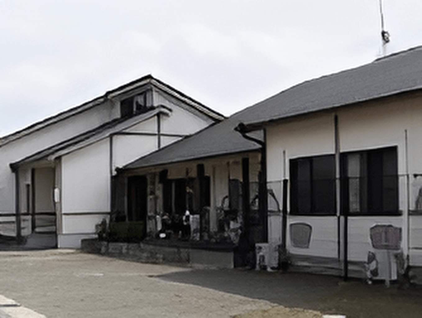 平屋建ての建物。外壁は白く、屋根はグレーで、三角屋根。日当たりのいい場所に建っている。