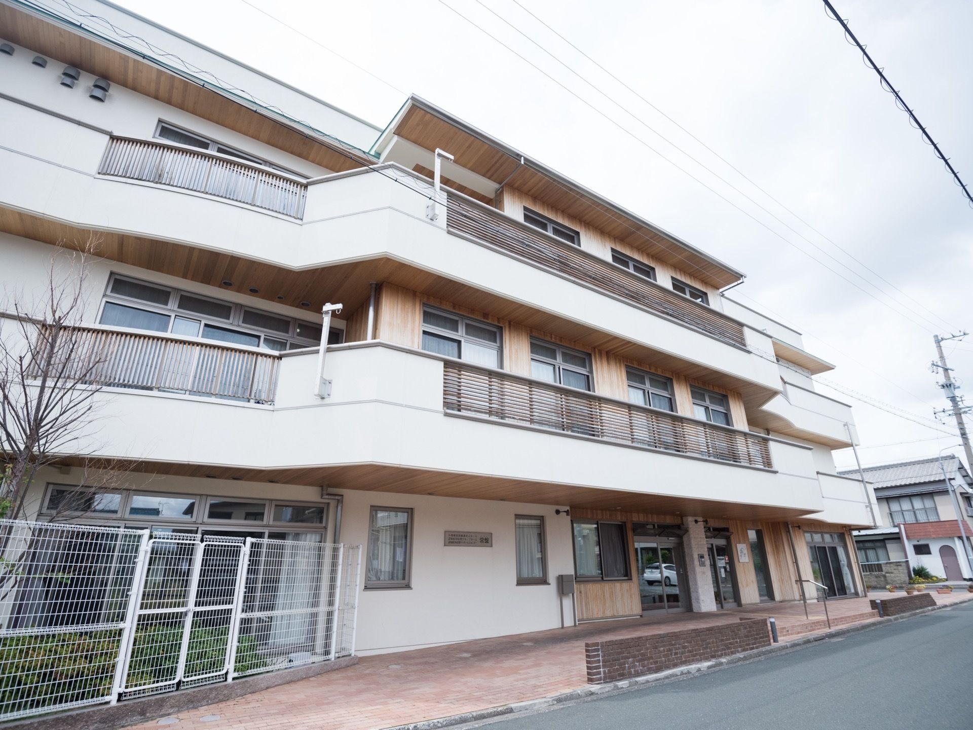 道路に面した３階建ての建物である。２、３階部分にはベランダが設置されている。１階部分には、フェンスがある。