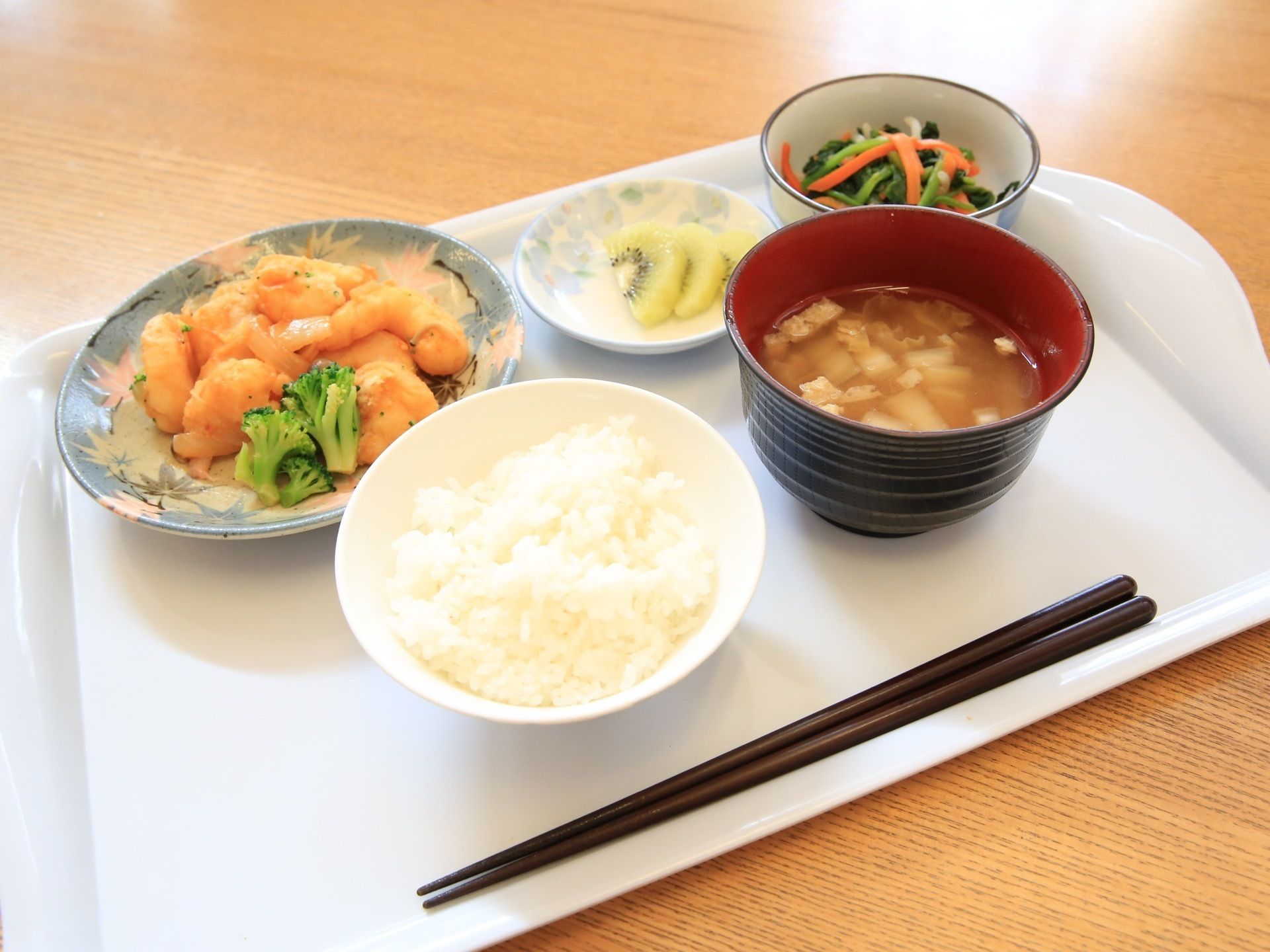 ある日の給食である。エビとブロッコリーの煮びたし、豆腐の味噌汁、野菜のおひたし、白ご飯、キュウイである。