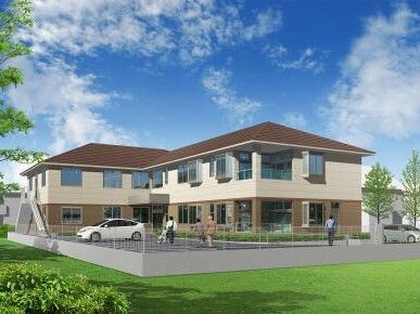 エル字型の建物はブラウン系の外観で2階建て。敷地内には駐車場があり、複数名の人が歩いている。