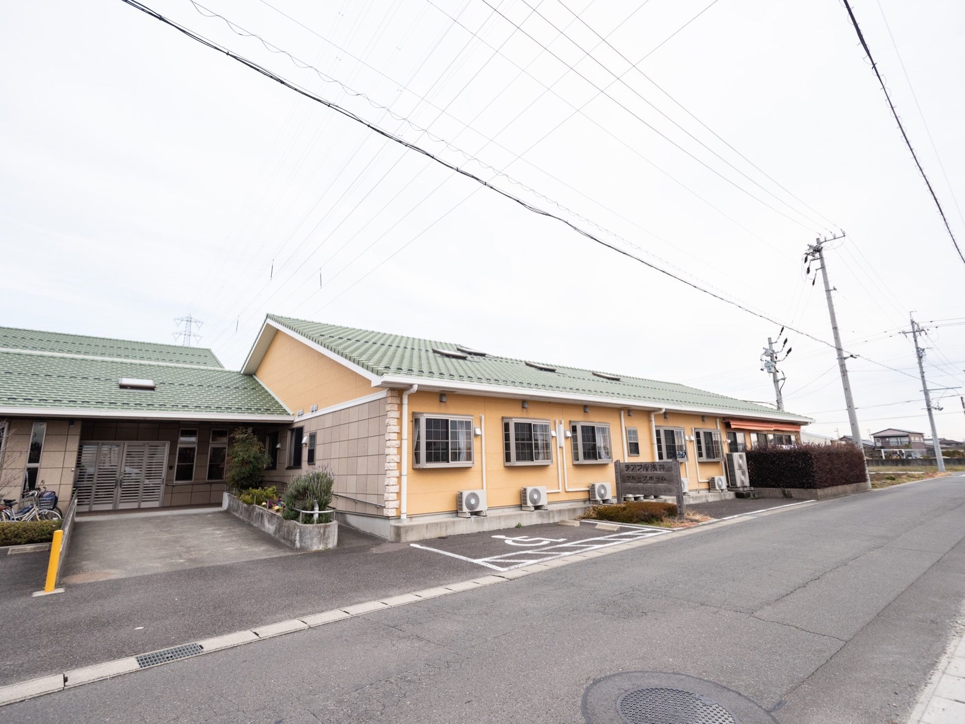 施設は平屋建ての建物で、玄関まではスロープ状になっている。車椅子マークが書かれた駐車スペースが用意されている。