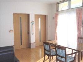 大きな窓にはカーテンとレースカーテンが付いていて、フロアには木製のダイニングテーブルが置かれ、二つのドアが並んでいる。