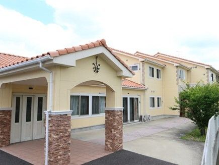 明るい雰囲気の2階建ての建物。オレンジ系の屋根が付き、窓もたくさんある。玄関には屋根があり、白くて大きな度が付いている。