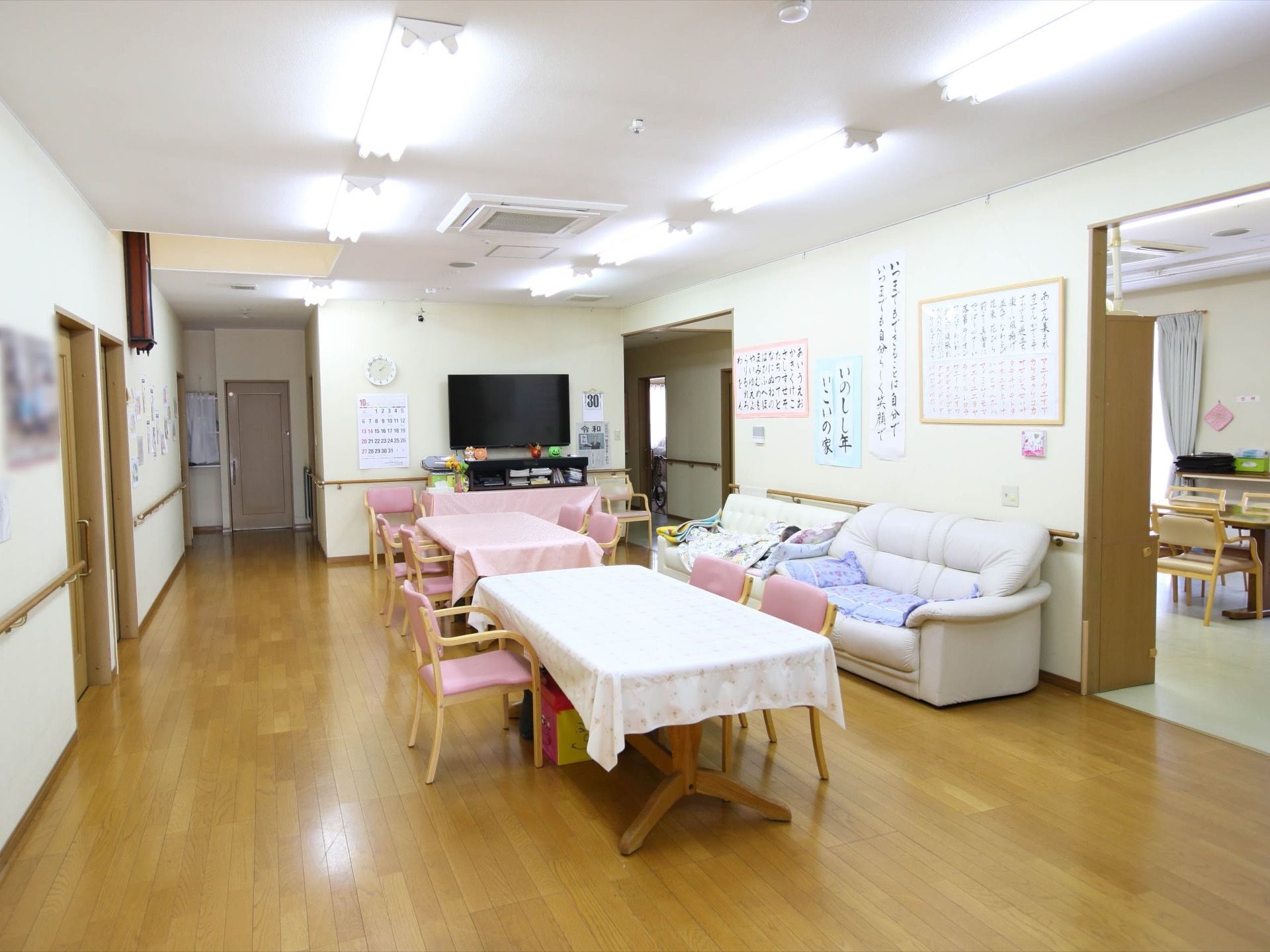中央にテーブルと椅子が並んでいる談話室。壁際には大きなソファが２つ置かれ、正面には大きなテレビがある。壁には手すりがある。