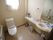 広く、開放感のあるトイレである。白色の洋式便座を完備している。手洗い場も備え付けられ、小物類を置くスペースもある。