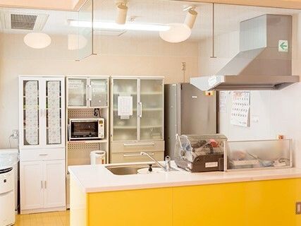 キッチンは対面式で、シンクのそばには食器乾燥機があり、奥には冷蔵庫や電子レンジ、食器棚などがある。