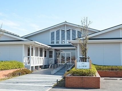 手すり付きのスロープが設置されている玄関の周りには草木が植えられている。平屋建ての建物は三角屋根も付いている。
