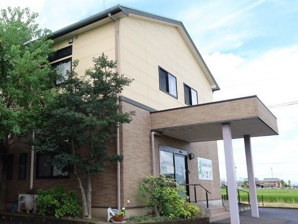 2階部分がベージュ、1階部分がブラウンの２階建ての建物は玄関先には手すり付きの階段と屋根がある。