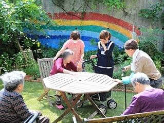 虹が描かれた壁が印象的な庭には木製のテーブルがあり、入居者がそれを囲むように数名立ったり座ったりしている。