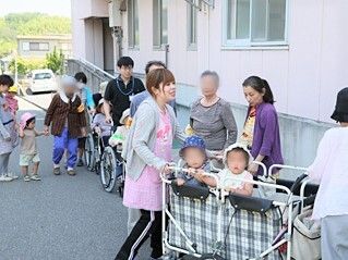 車いすの入居者も一緒に散歩に出かけている様子。園児たちは歩いている子もいれば、カートの中に入っている子もいる。