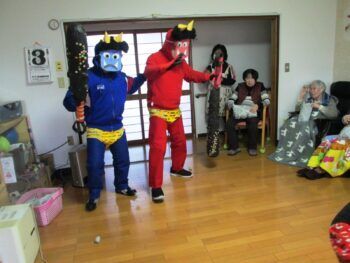 赤鬼や青鬼になったスタッフが金棒を持って現れ、高齢者が鬼に向かって何かを投げている。