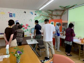 共有スペースの長机に並べられた展示品を真剣に見ている人たち。中央にあるテーブルにはお茶が用意されている。