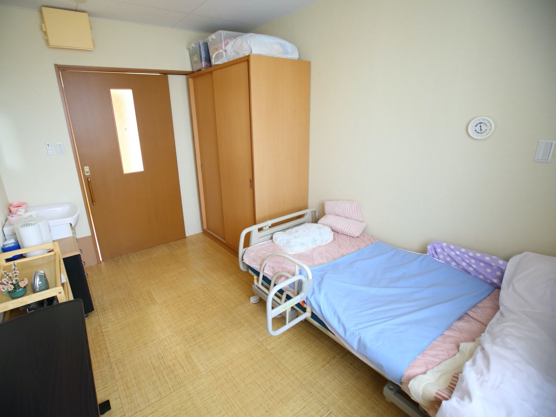 介助バーが装着された介護用ベッドや収納タンスが設置された居室である。入居者様のお好みにレイアウトされている。